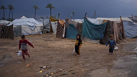 أطفال فلسطينيون نازحون يسيرون عبر مخيم خيام غارق بالمياه عقب هطول أمطار غزيرة في دير البلح، وسط قطاع غزة، الثلاثاء 24 فبراير/شباط 2026. (صورة من وكالة أسوشيتد برس/عبد الكريم ح